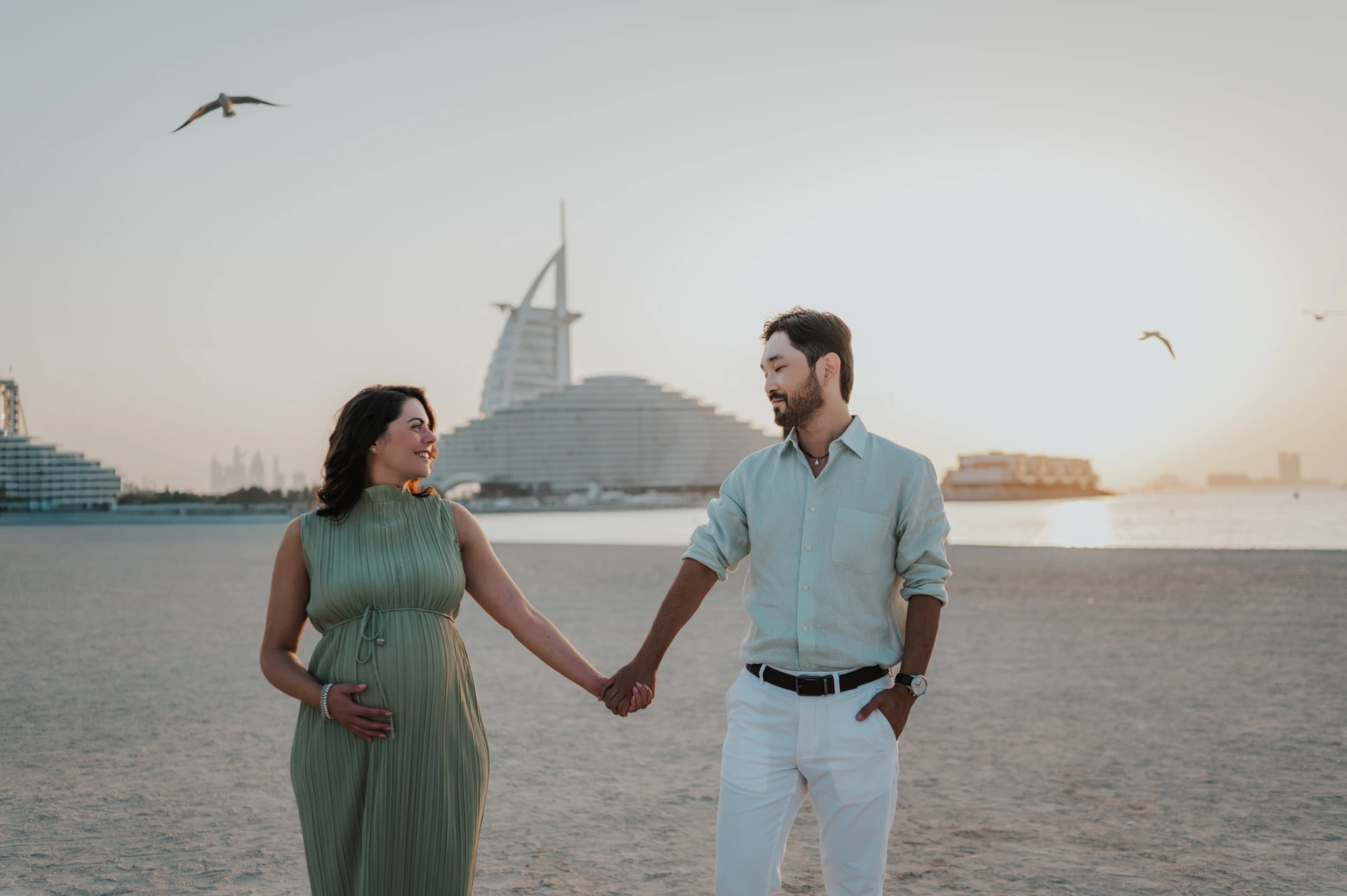 An expecting couple stands together on Dubai beach near Burj Al Arab, illustrating weekday timing guidance for a maternity photoshoot.