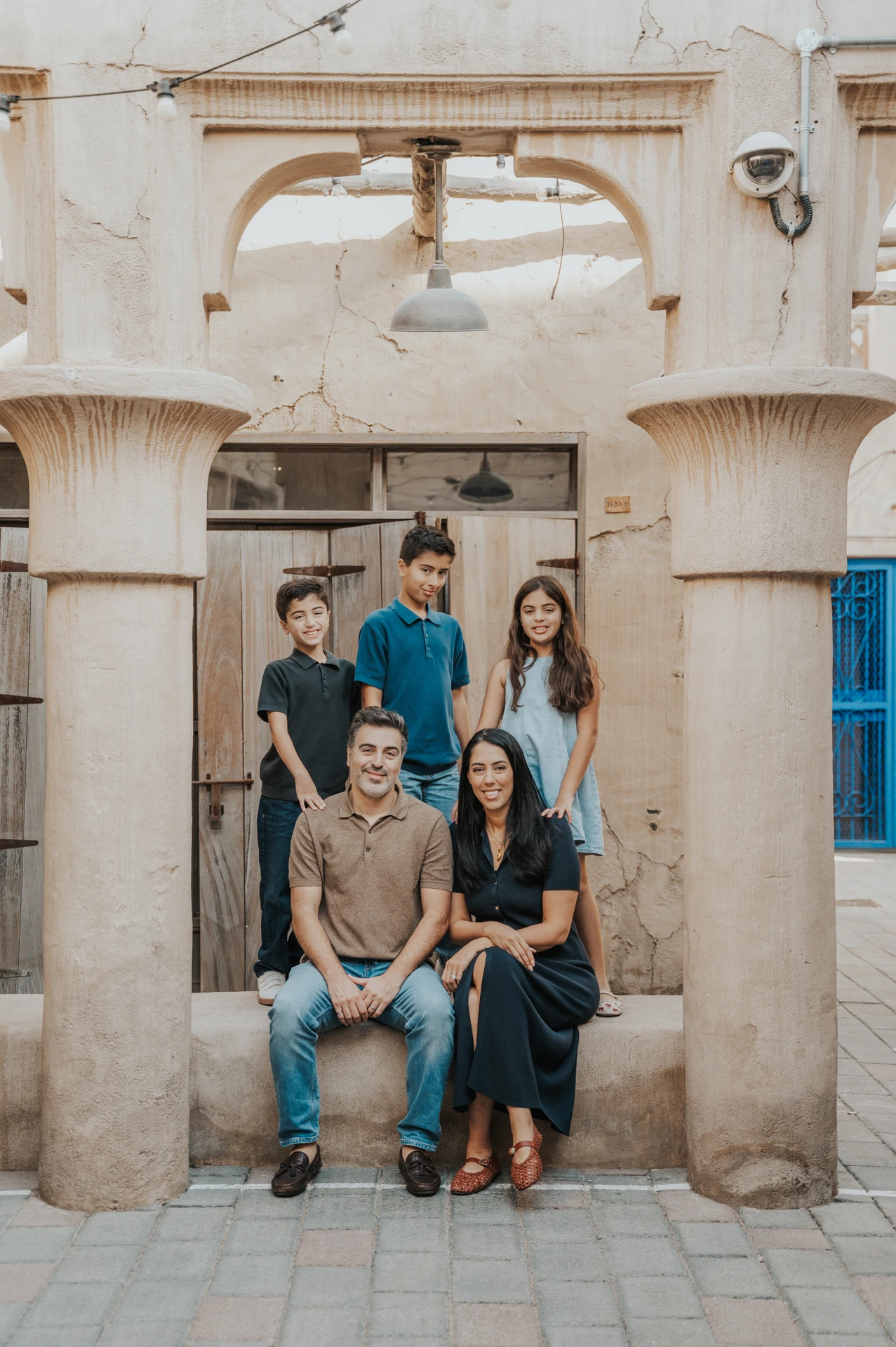 A family poses in Old Dubai architecture during a vacation family photoshoot, framed by textured stone columns and traditional urban heritage details.
