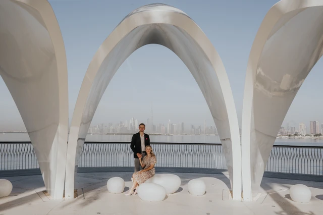 A couple poses under a modern Dubai landmark arch, showing coordinated outfit styling for sunrise or sunset sessions.